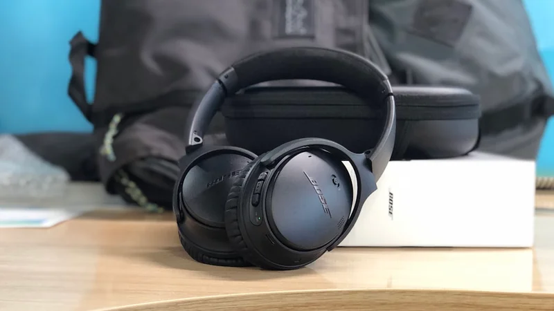 Bose QuietComfort Ultra headphones on wooden desk with warm studio lighting, premium ANC headphones close-up