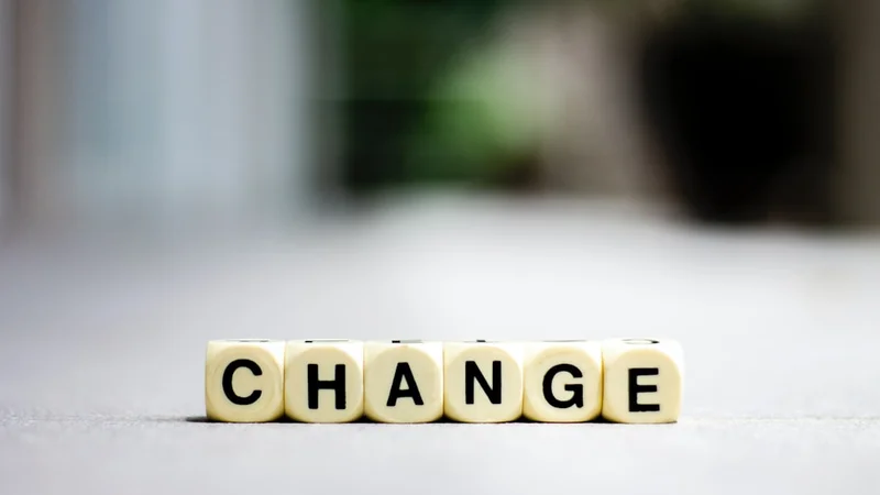 Overhead flat-lay of a plain open notebook and a pen on a minimal desk, with three short handwritten headings: "What changed," "What I'm updating," "What I'm doing" — the change journal practice