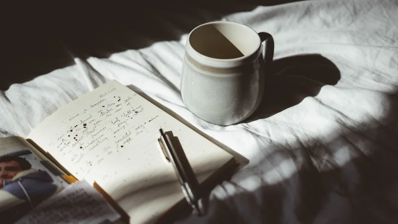 Hands wrapped around a white mug, a journal open on a wooden table with morning light streaming through the window