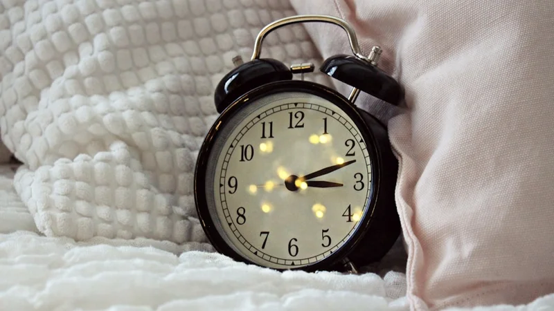 person sitting up in bed at dawn, morning sunlight streaming through a window, looking rested and clear-eyed