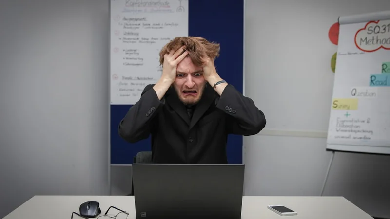 A person at a desk gripping a phone with both hands, eyes fixed on the screen, shoulders tense — warm late-afternoon apartment light, urban setting, anxious and focused expression