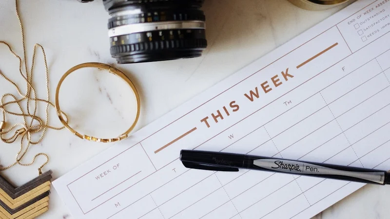 A flat-lay of a clean wooden desk with an open planner, a pen, and a small notebook — morning light falling across the surface