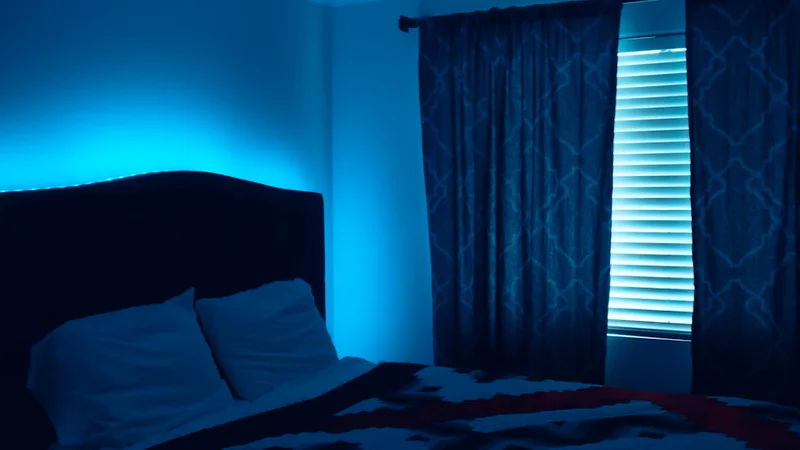 A dim bedroom at night with moonlight falling on a tangled duvet and a small lamp glowing softly on the bedside table