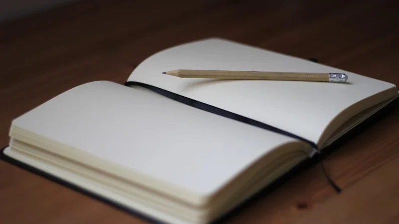 Warm overhead view of a person's hands holding an open journal on a wooden table, morning light streaming in from a window, writing thoughtfully
