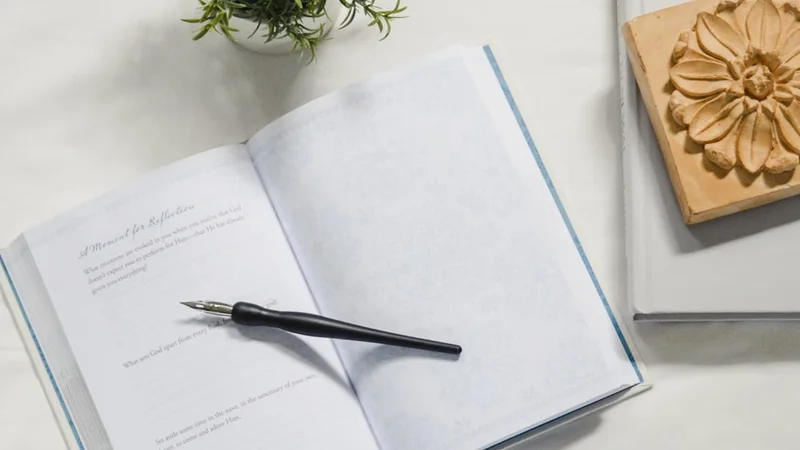 A calm overhead view of a small desk workspace with a journal open, pen resting on it, representing the observer's perspective and the practice of self-distancing through writing