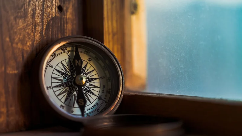 A vintage compass resting on a wooden windowsill in warm afternoon light, its needle steady against the grain