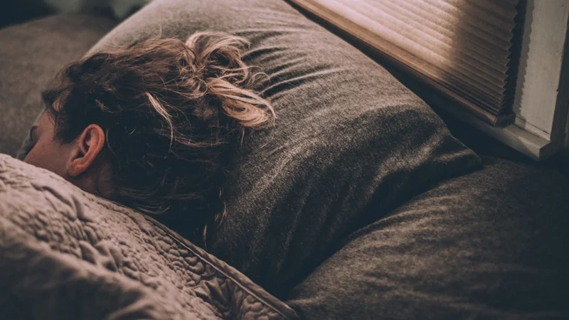 Clean, minimal bedroom environment — no screens, blackout curtains drawn, cooling device visible, warm amber lamp on low, serene and purposeful sleep setup