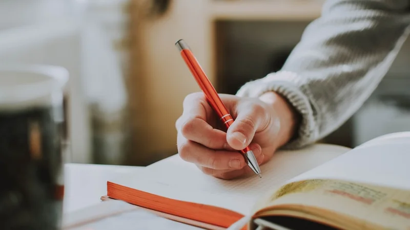 A person writing in a journal at a desk with a warm beverage nearby, reviewing their performance thoughtfully