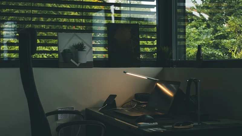 person sitting alone at a dimly lit office desk, staring at an empty chair across from them, expression uncertain