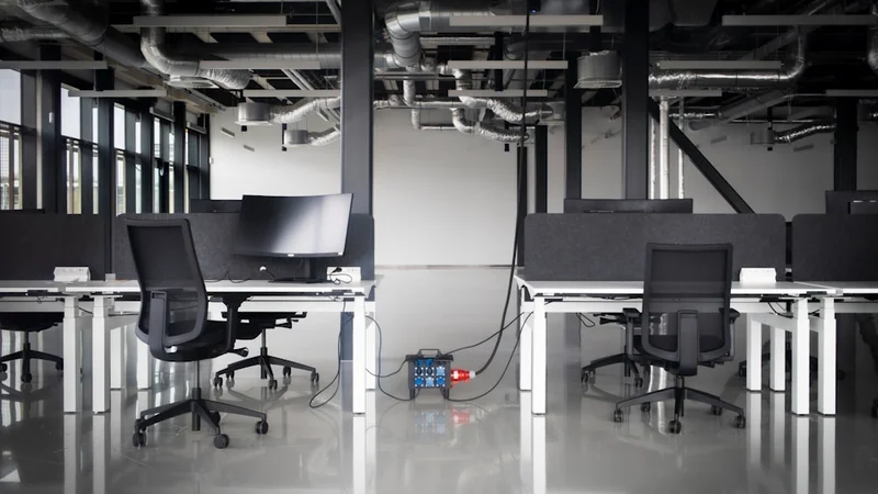 two colleagues in a bright open-plan office, one presenting a document while the other turns away dismissively